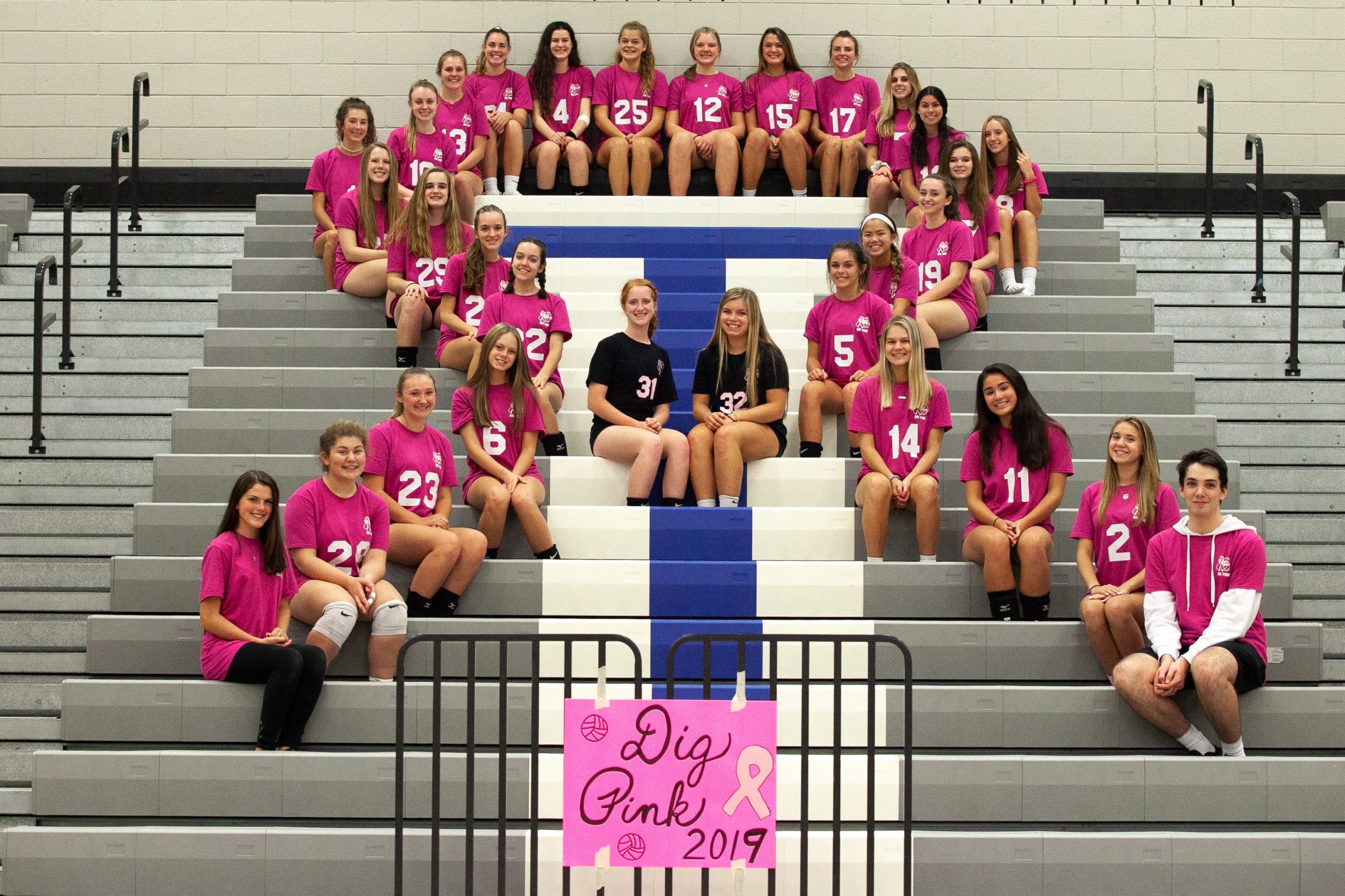 Team members sit on the school bleachers in a breast cancer ribbon formation.